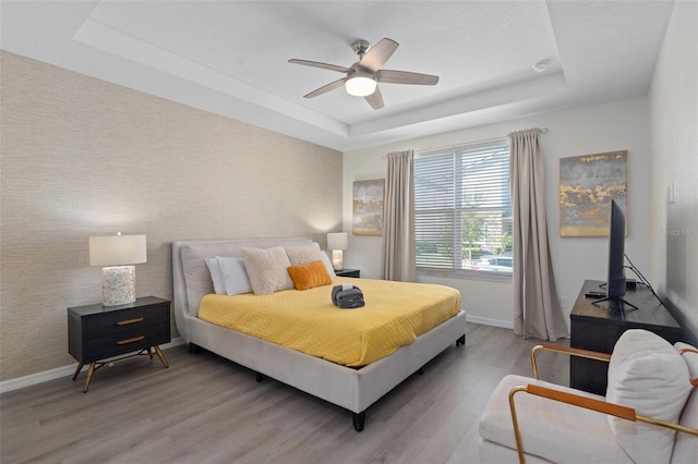 bedroom featuring a raised ceiling, ceiling fan, a textured ceiling, and light wood-type flooring