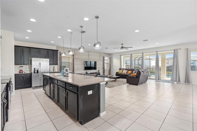 kitchen featuring light stone countertops, appliances with stainless steel finishes, ceiling fan, pendant lighting, and a center island with sink