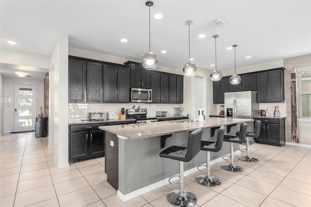 kitchen with a kitchen island with sink, a kitchen breakfast bar, appliances with stainless steel finishes, decorative light fixtures, and light stone counters