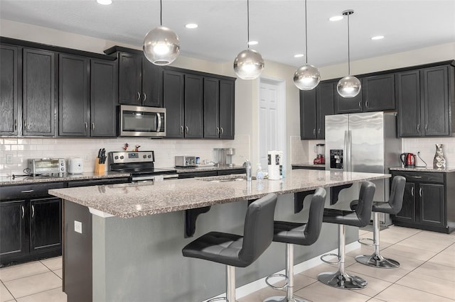 kitchen with light stone countertops, hanging light fixtures, appliances with stainless steel finishes, and an island with sink