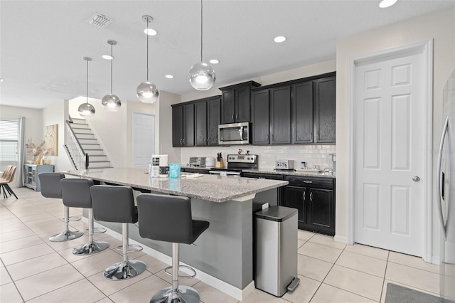 kitchen with pendant lighting, a center island with sink, light stone counters, appliances with stainless steel finishes, and a kitchen bar