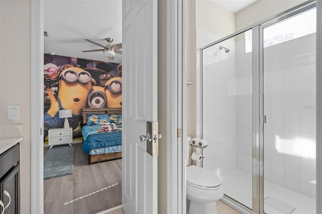 bathroom with ceiling fan, wood-type flooring, toilet, a shower with door, and vanity