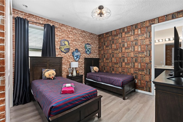 bedroom featuring ensuite bathroom, a textured ceiling, brick wall, and light hardwood / wood-style flooring