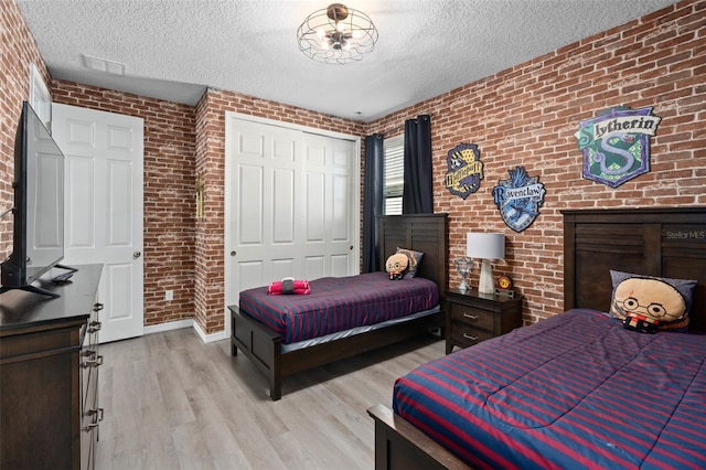 bedroom featuring a closet, light hardwood / wood-style flooring, brick wall, and a textured ceiling