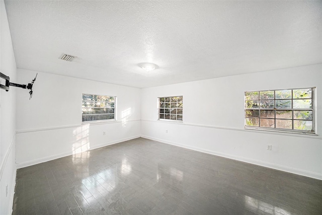 empty room featuring a textured ceiling, dark hardwood / wood-style flooring, and plenty of natural light