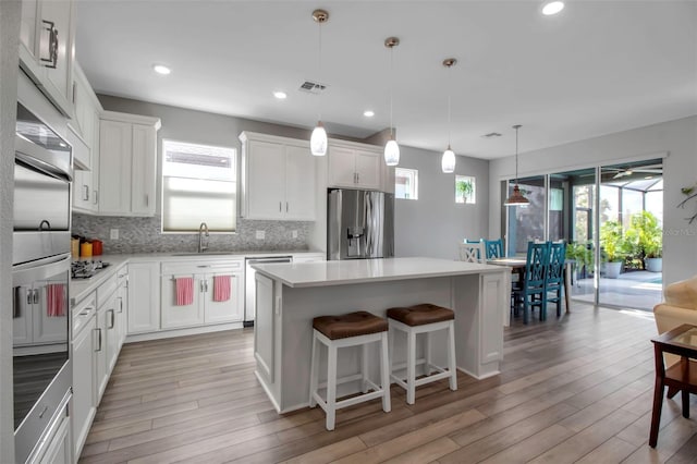 kitchen with decorative light fixtures, white cabinets, stainless steel appliances, and a kitchen island