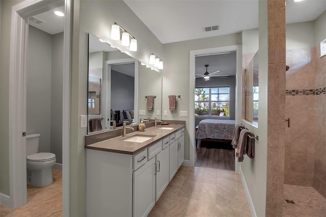 bathroom with toilet, tile patterned flooring, tiled shower, vanity, and ceiling fan