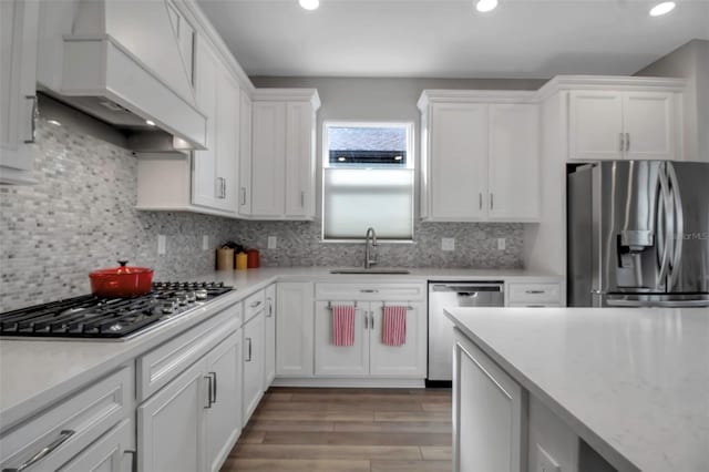 kitchen featuring sink, white cabinetry, appliances with stainless steel finishes, custom range hood, and decorative backsplash