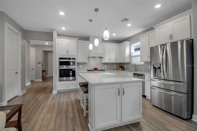 kitchen featuring a kitchen island, appliances with stainless steel finishes, decorative light fixtures, white cabinetry, and sink