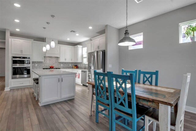 kitchen with appliances with stainless steel finishes, a kitchen island, white cabinetry, decorative backsplash, and hanging light fixtures