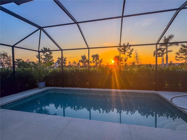 pool at dusk featuring a lanai and a patio