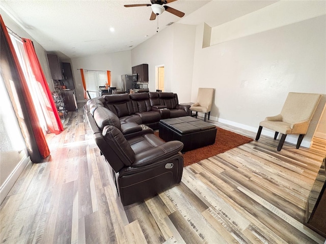 living room with ceiling fan, light hardwood / wood-style floors, and high vaulted ceiling