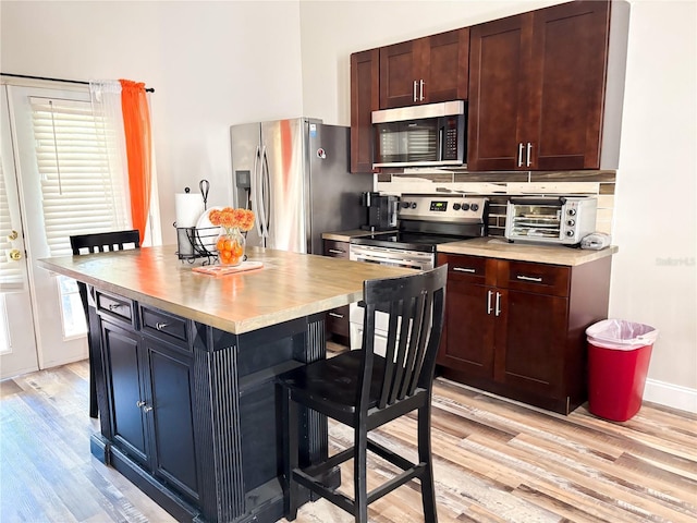 kitchen featuring a breakfast bar, a center island, backsplash, light hardwood / wood-style flooring, and appliances with stainless steel finishes