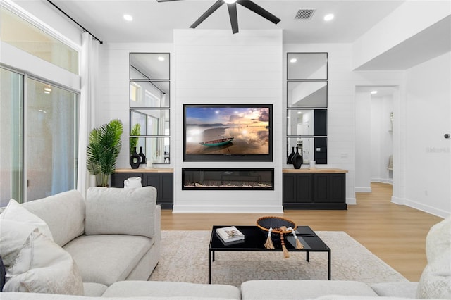 living room featuring ceiling fan, a fireplace, and light hardwood / wood-style floors