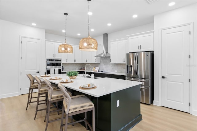 kitchen featuring white cabinets, a center island with sink, wall chimney exhaust hood, and stainless steel appliances