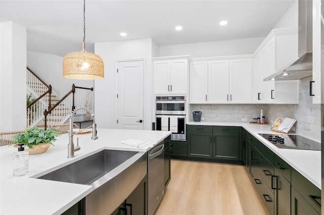 kitchen with white cabinetry, hanging light fixtures, wall chimney range hood, light hardwood / wood-style floors, and appliances with stainless steel finishes