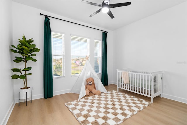 bedroom with ceiling fan, a nursery area, and light hardwood / wood-style floors