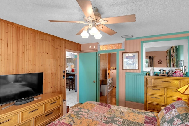 bedroom with ceiling fan, wood walls, light tile patterned floors, and a textured ceiling