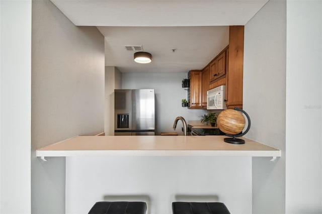 kitchen featuring a kitchen breakfast bar, kitchen peninsula, sink, and stainless steel refrigerator with ice dispenser