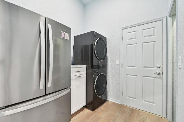 washroom with cabinets, stacked washer and clothes dryer, and light wood-type flooring