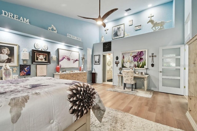 bedroom featuring ceiling fan, ensuite bath, a high ceiling, and light hardwood / wood-style flooring