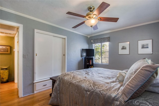 bedroom with ceiling fan, light wood-type flooring, ornamental molding, and a closet