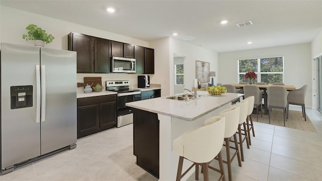 kitchen featuring dark brown cabinetry, sink, an island with sink, a breakfast bar, and appliances with stainless steel finishes