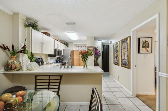 kitchen featuring white cabinetry, a kitchen bar, kitchen peninsula, and a textured ceiling