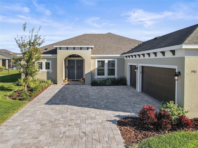 view of front of property with a shingled roof, an attached garage, fence, and stucco siding