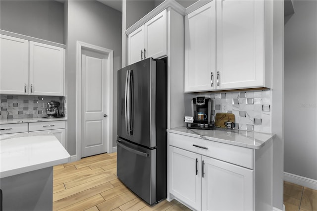 kitchen with decorative backsplash, white cabinetry, stainless steel refrigerator, and light stone counters