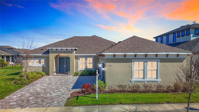 view of front of house featuring a shingled roof, decorative driveway, a yard, and stucco siding