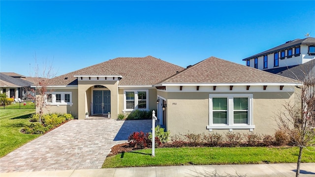 view of front of house featuring a front yard, decorative driveway, roof with shingles, and stucco siding