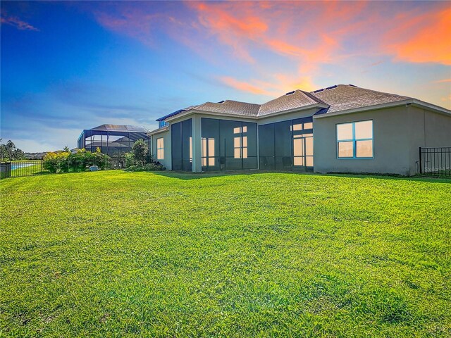 rear view of house featuring stucco siding, a lawn, roof with shingles, and fence