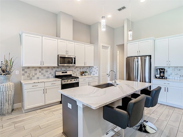 kitchen with visible vents, a sink, appliances with stainless steel finishes, pendant lighting, and a kitchen bar