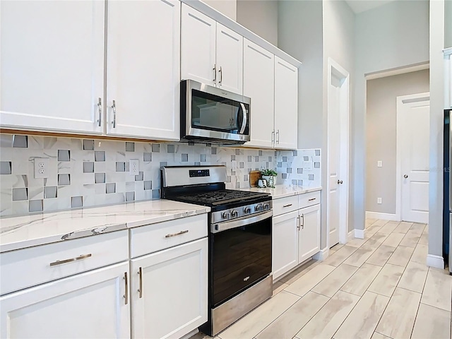 kitchen with baseboards, light stone counters, decorative backsplash, appliances with stainless steel finishes, and white cabinets