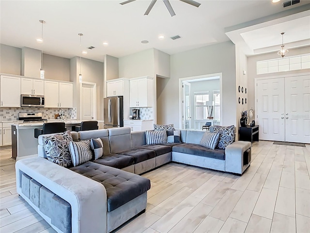 living area with visible vents, a high ceiling, ceiling fan, and light wood finished floors