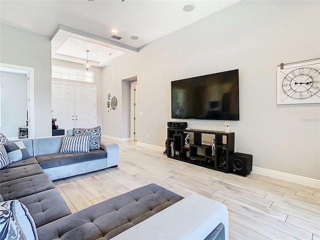 living area with a tray ceiling, visible vents, baseboards, and wood tiled floor