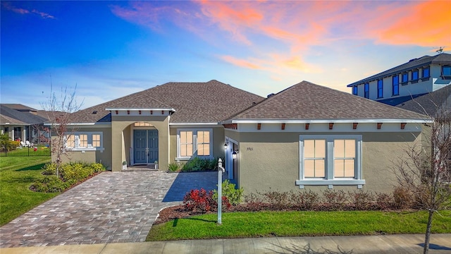 view of front of house with a front lawn, decorative driveway, roof with shingles, and stucco siding