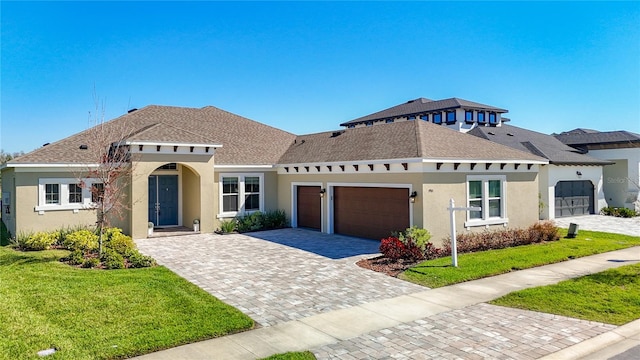 mediterranean / spanish-style house featuring a front yard, roof with shingles, stucco siding, decorative driveway, and an attached garage
