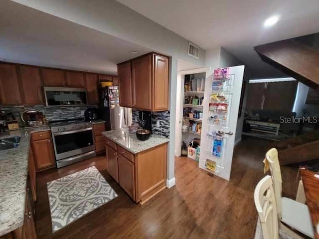 kitchen with decorative backsplash, appliances with stainless steel finishes, light stone countertops, dark wood-type flooring, and sink