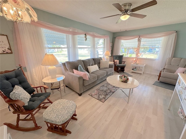 living room featuring ceiling fan with notable chandelier, light hardwood / wood-style floors, and a textured ceiling