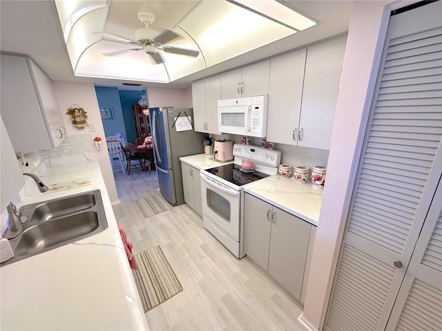 kitchen with white appliances, a tray ceiling, sink, white cabinets, and light hardwood / wood-style floors