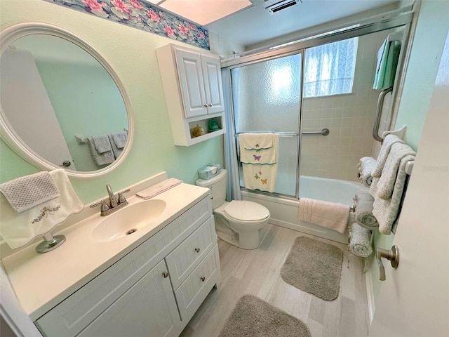 full bathroom with shower / bath combination with glass door, hardwood / wood-style floors, vanity, and toilet