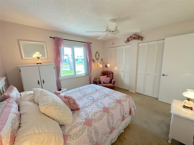 bedroom with a textured ceiling, ceiling fan, light carpet, and multiple closets