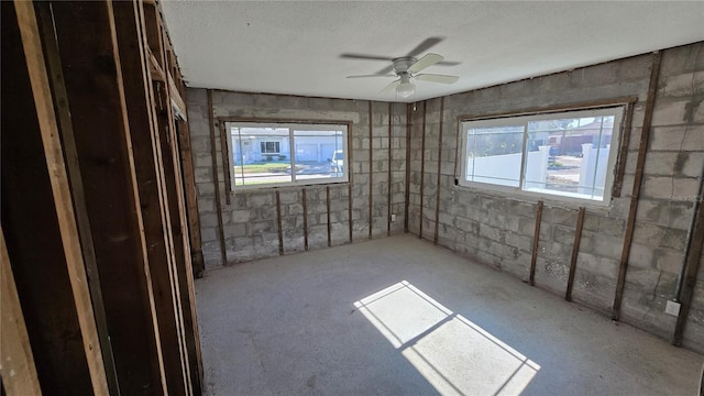 spare room featuring a ceiling fan, a textured ceiling, and concrete block wall
