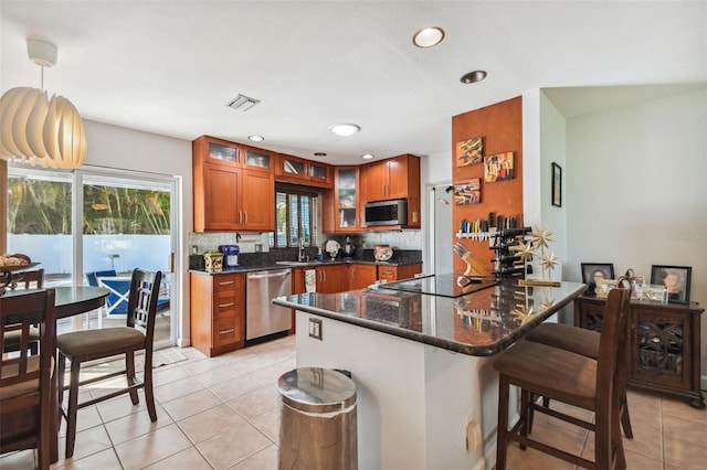 kitchen with brown cabinets, a breakfast bar, glass insert cabinets, light tile patterned floors, and stainless steel appliances