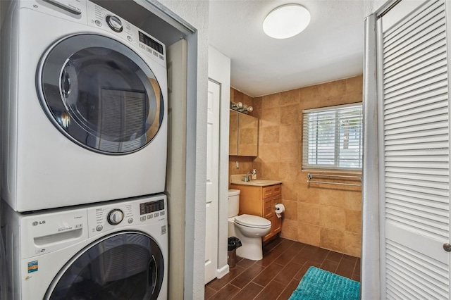 laundry area with a sink, tile walls, stacked washer / drying machine, wood finish floors, and laundry area