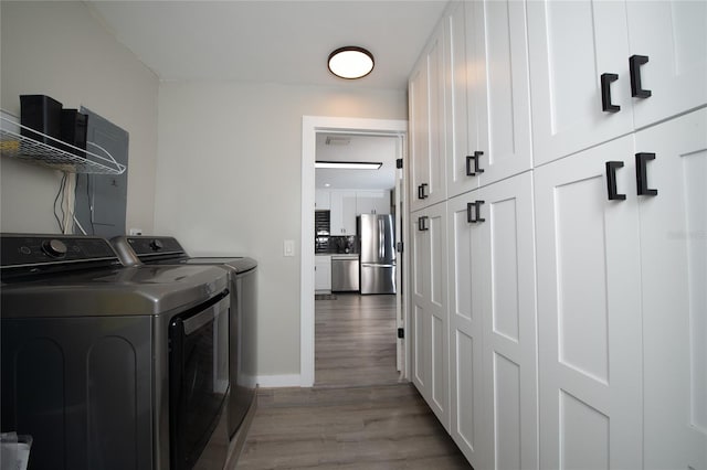 laundry area featuring washing machine and clothes dryer, hardwood / wood-style floors, and cabinets