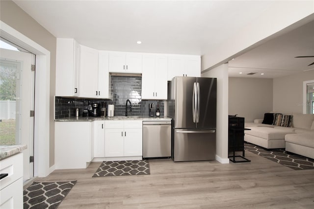 kitchen with light stone countertops, light hardwood / wood-style flooring, backsplash, white cabinets, and appliances with stainless steel finishes