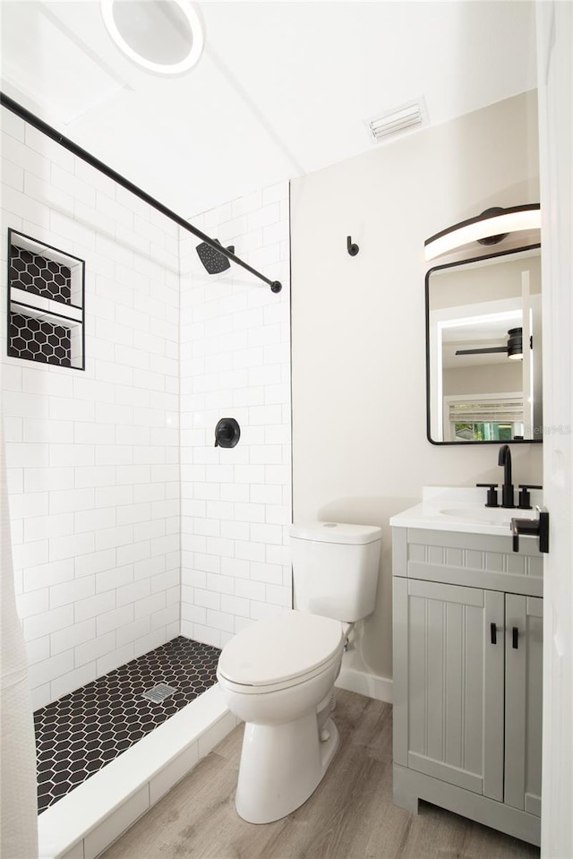 bathroom with tiled shower, hardwood / wood-style floors, vanity, and toilet